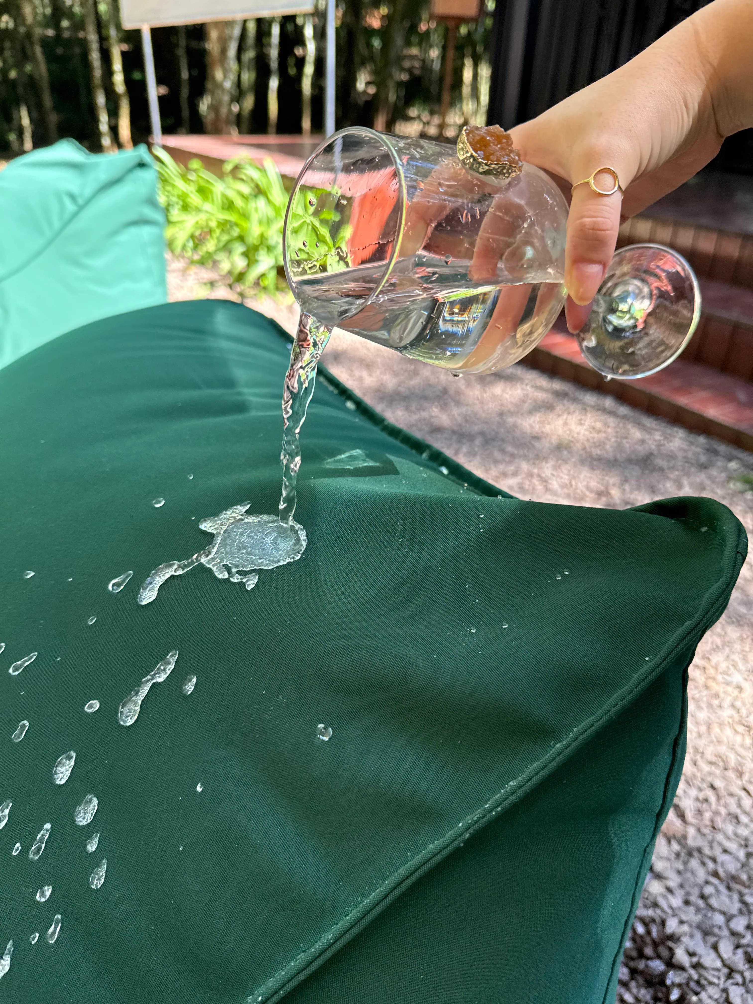 Água escorrendo sobre o tecido verde de um puff Damie Garden, demonstrando repelência à água