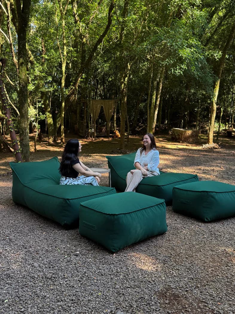 Duas pessoas conversando sentadas em espreguiçadeira e puff Damie Garden na cor verde, em ambiente externo